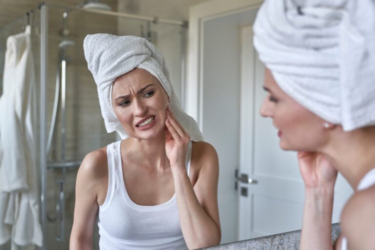 woman holding her jaw in the mirror, suffering from bruxism and TMJ related pain