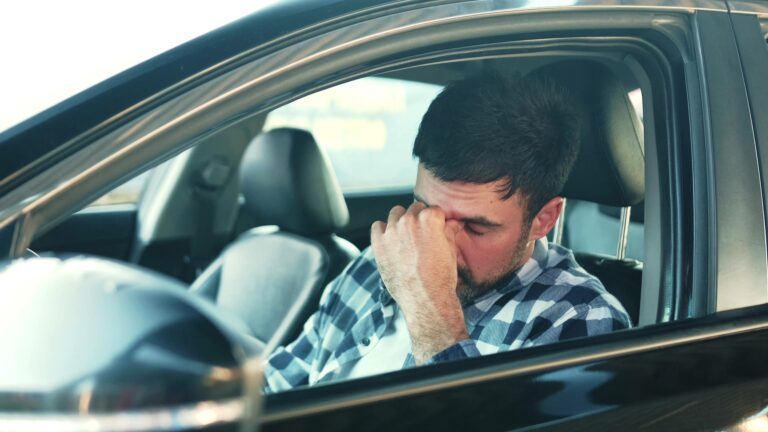 young man feeling stressed, sitting at driver seat in a car.