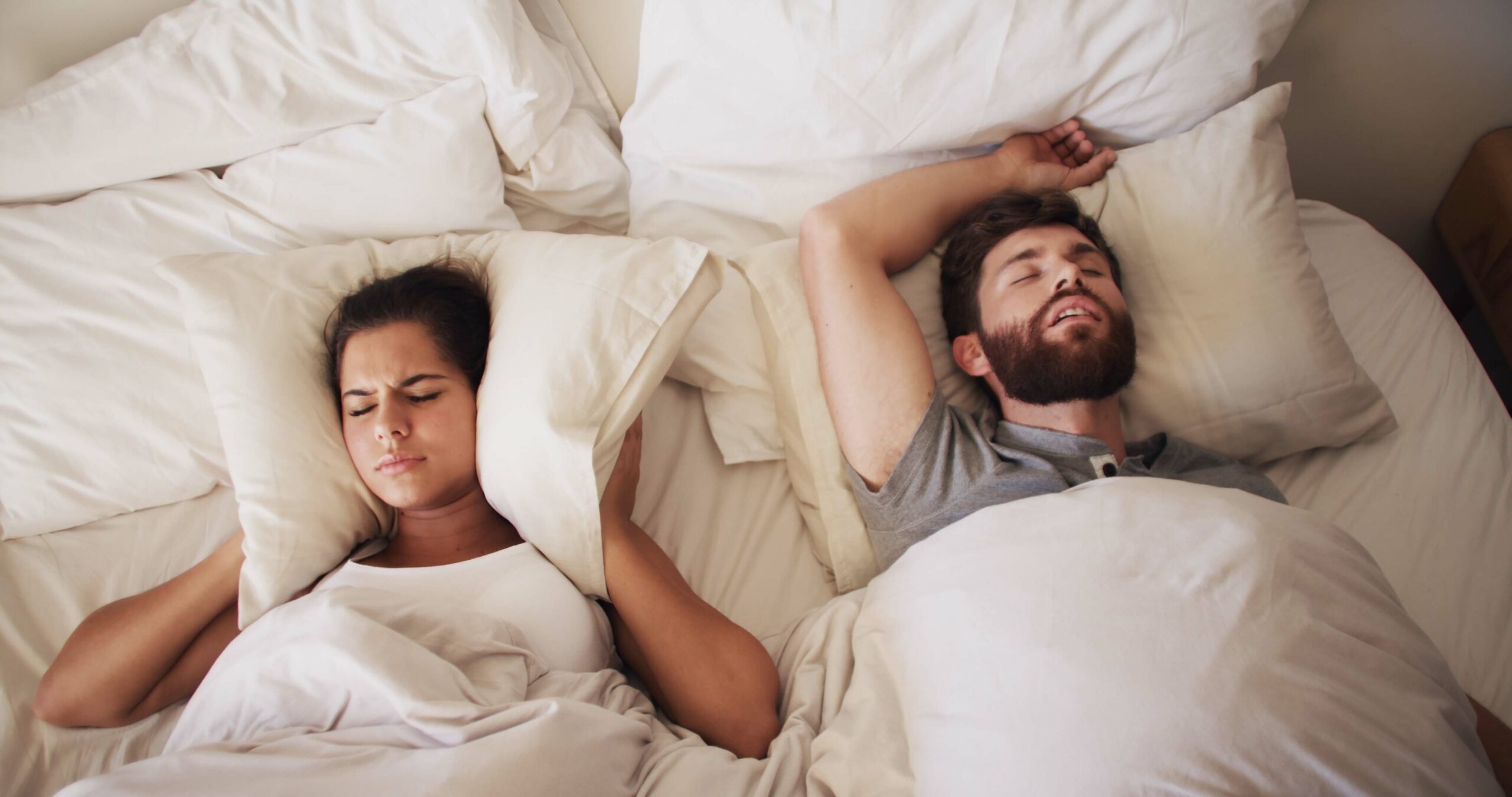 man snoring, woman covering her ears with pillow, snoring or sleep apnea sufferer