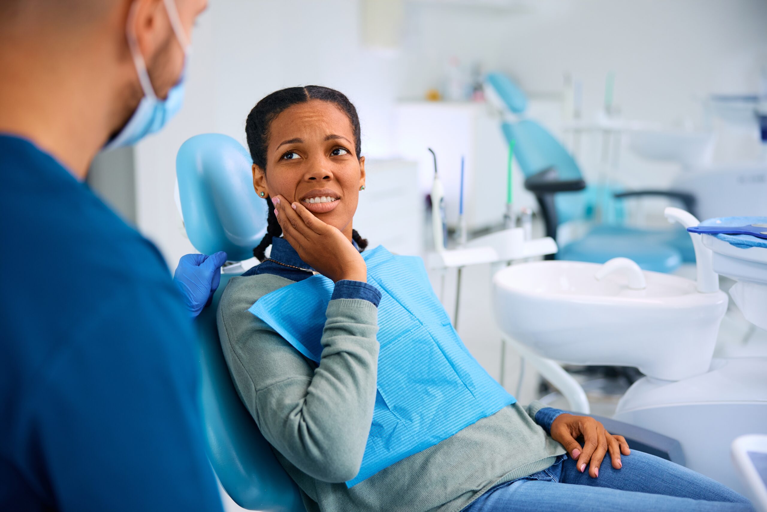 young woman sitting in a dental chair complaining of TMJ pain