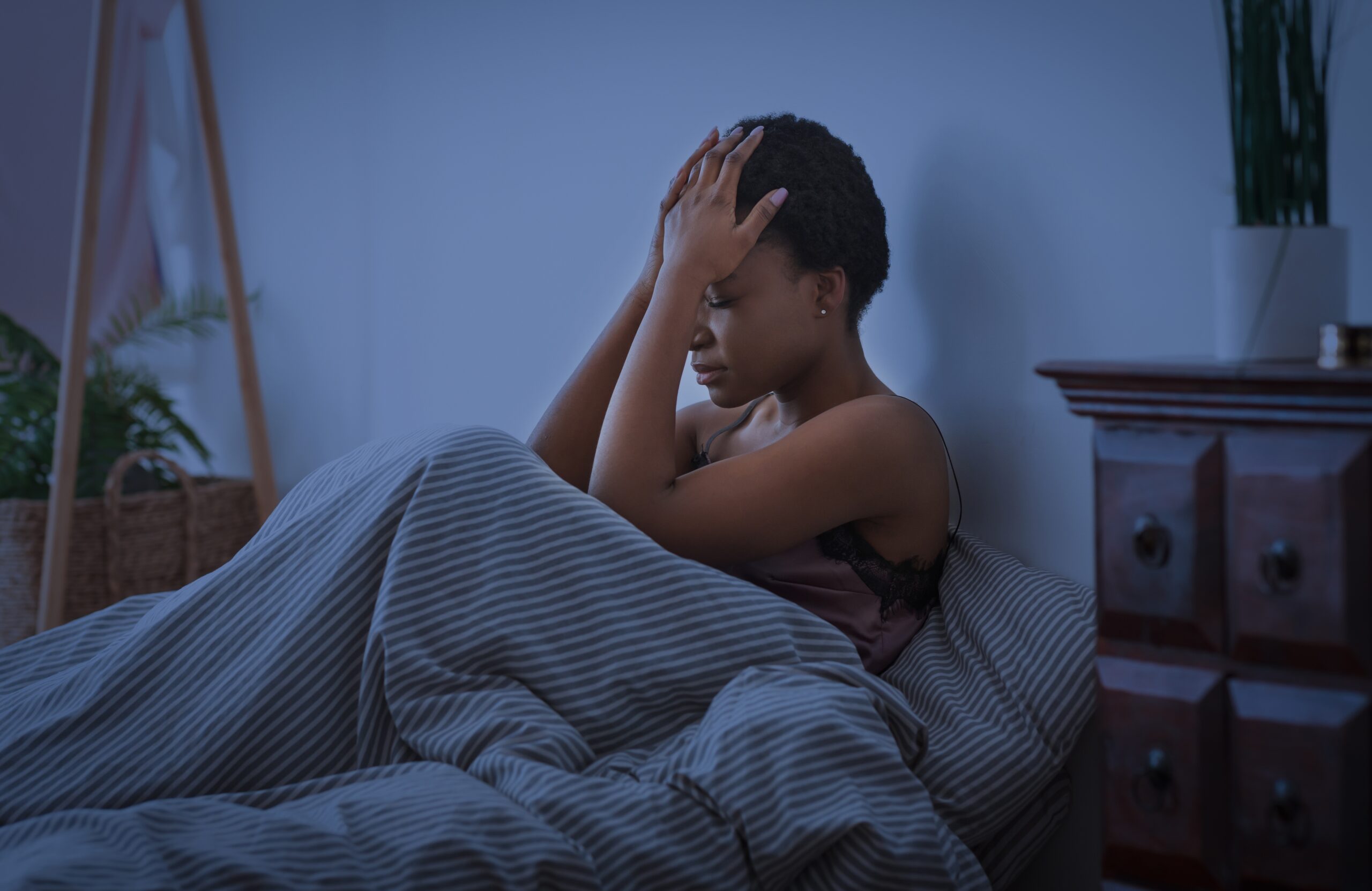 woman sitting up in bed with her hands on head, struggling to sleep