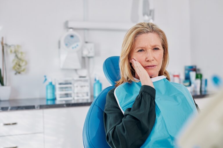 older woman suffering from TMJ pain, sitting in dental chair