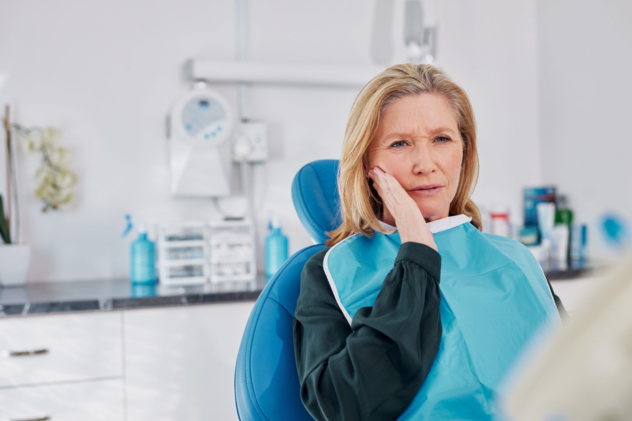 older woman suffering from TMJ pain, sitting in dental chair